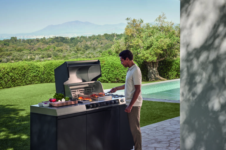 miele-outdoorküche-dreams-mann-am-grillen-hintergrund-graslandschaft